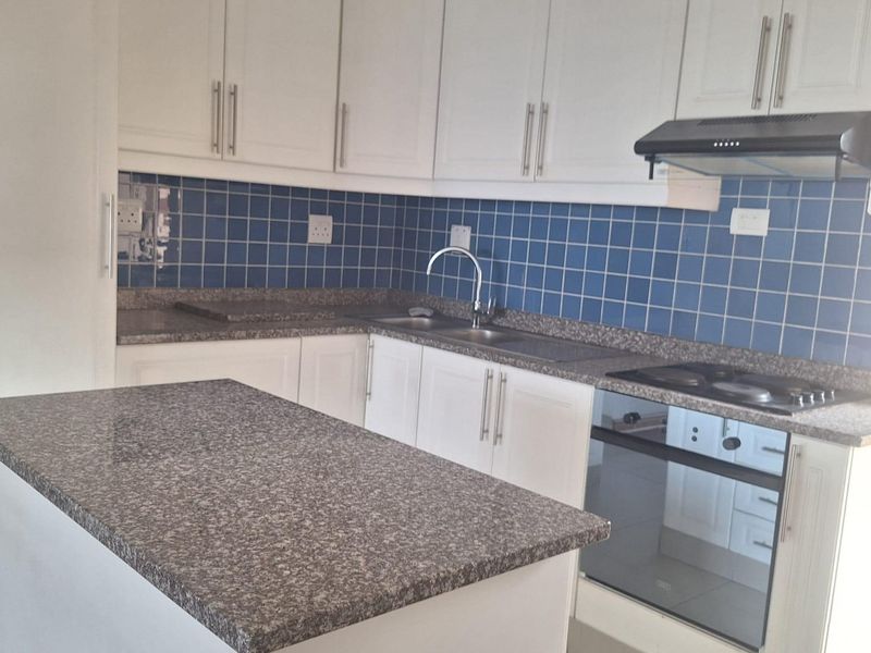A clean, functional kitchen featuring white cabinetry, granite countertops, a blue tiled backsplash, and integrated appliances including an oven and hob.