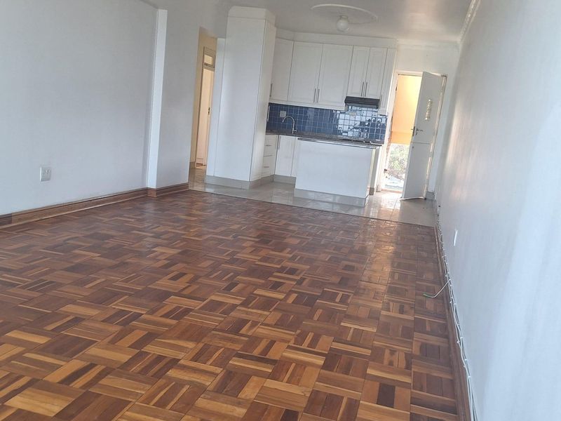 Open-plan living area featuring traditional parquet flooring, leading into a compact kitchen with built-in cabinetry and tiled backsplash.