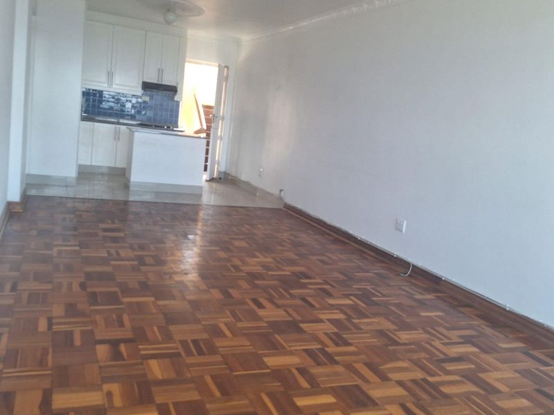 An open-plan living area featuring classic parquet flooring, white walls with decorative coving, and a compact kitchen with built-in cabinetry and a tiled backsplash.