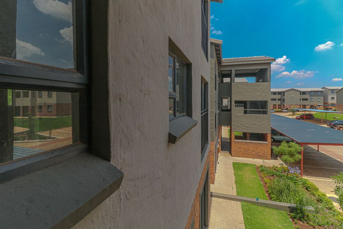 Exterior view of the apartment complex featuring brick and plaster facade, aluminium windows, paved walkways, and covered parking bays.
