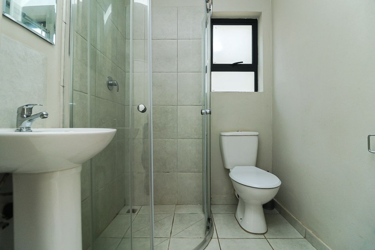 A functional bathroom featuring a pedestal basin, a glass-enclosed shower, and a standard toilet with neutral ceramic tiling throughout.