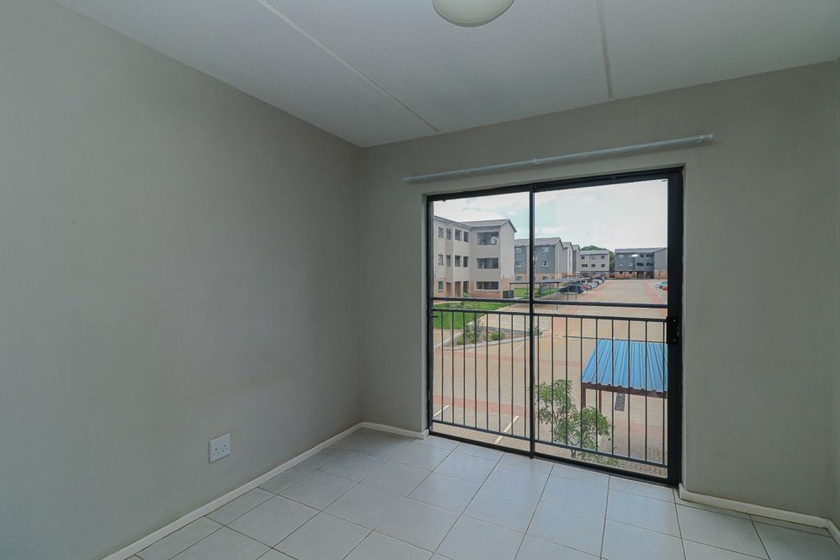An empty bedroom featuring neutral wall paint, tiled flooring, and a sliding glass door with a security gate leading to an exterior view.