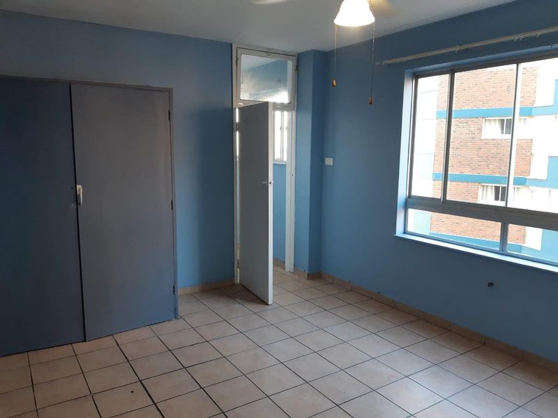 An empty bedroom featuring blue walls, tiled flooring, a built-in cupboard, and a large window providing natural light.