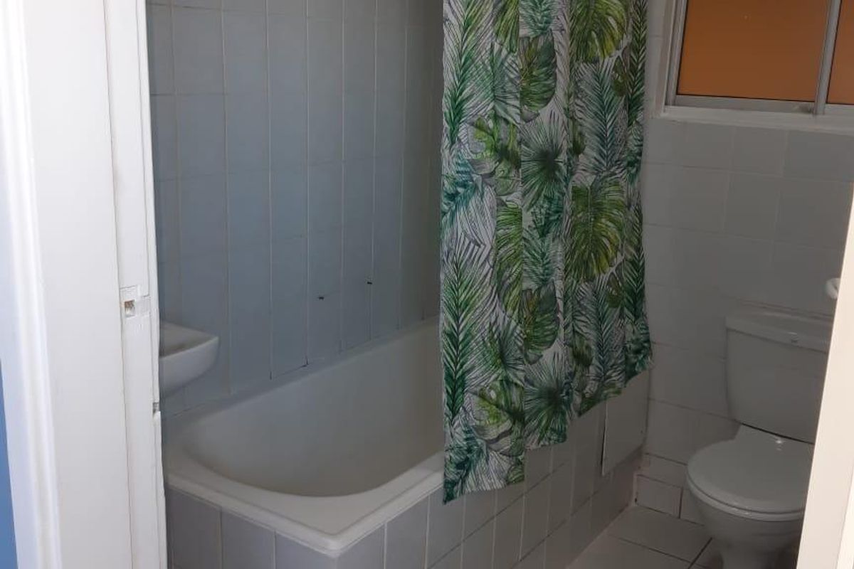 A functional bathroom featuring a bathtub with tiled surround, a standard toilet, and tiled flooring, requiring some cosmetic updates to the wall finishes.