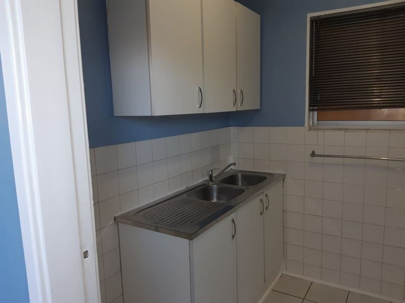 A functional scullery or utility area featuring white cabinetry, a stainless steel double sink, and tiled splashbacks.