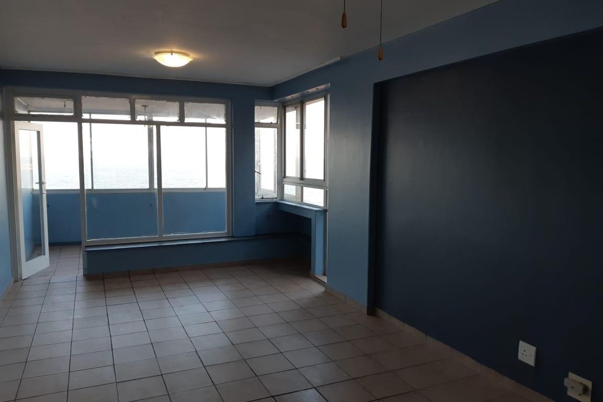 An empty, open-plan living area featuring tiled flooring, large windows with natural light, and a built-in window ledge overlooking the exterior.