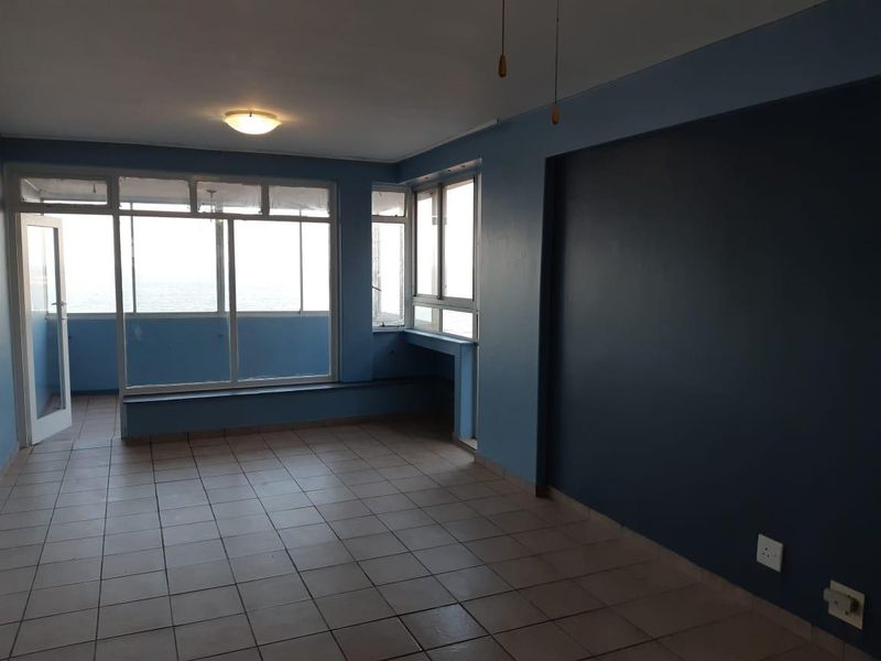 An empty, open-plan living area featuring tiled flooring, large windows with natural light, and a built-in window ledge overlooking the exterior.