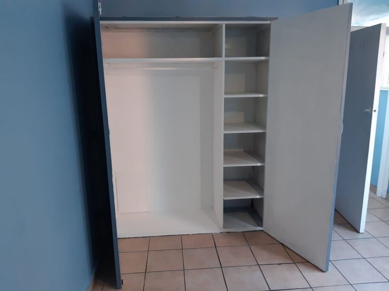 A bedroom featuring a built-in wardrobe with shelving and hanging space, finished with ceramic floor tiles.