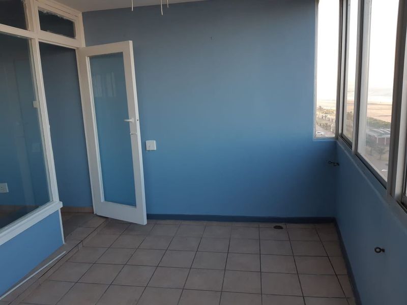 An empty, enclosed balcony space featuring tiled flooring, large windows with coastal views, and blue painted walls.