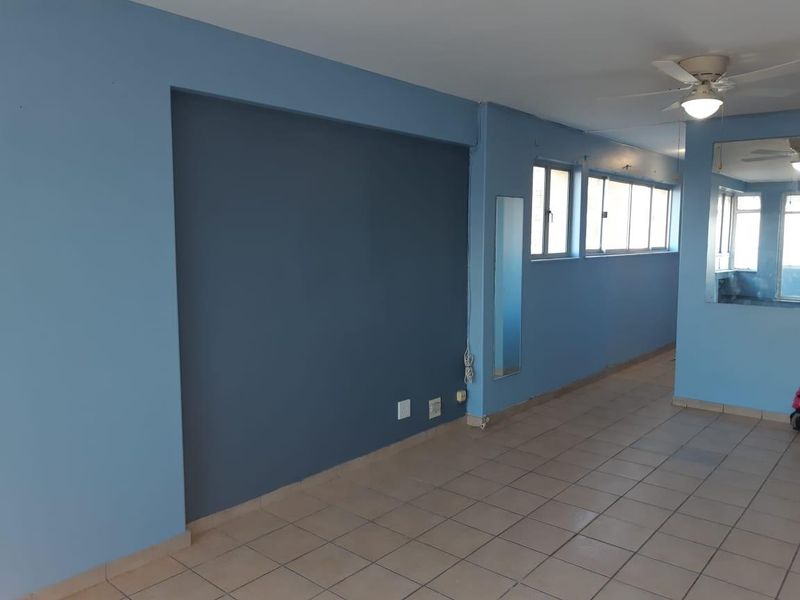 An empty living area featuring tiled flooring, a ceiling fan, and large windows, offering a blank canvas for interior design.