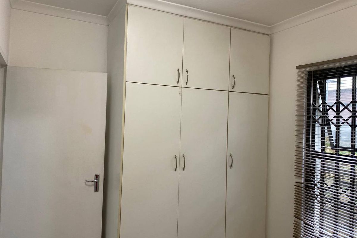 A bedroom featuring built-in cupboards, a window with security bars and venetian blinds, and standard interior finishes.