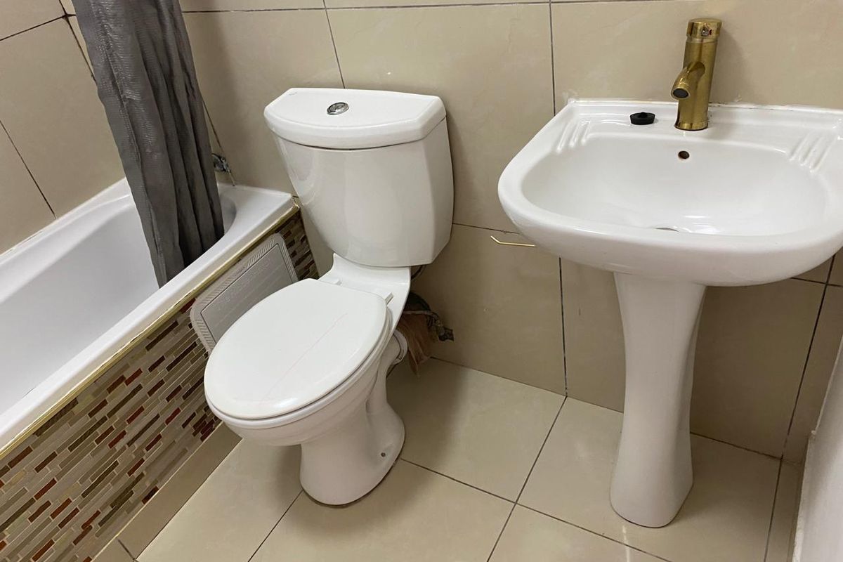 A functional bathroom featuring a pedestal washbasin with brass tap, a standard toilet, and a bathtub with tiled surround and mosaic accent detailing.