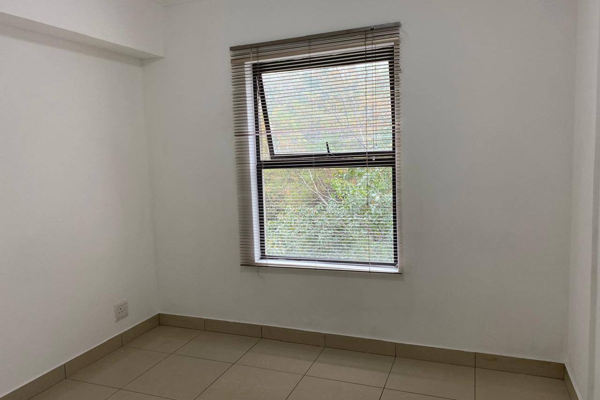 A clean, empty bedroom featuring neutral tiled flooring, white walls, and a window fitted with venetian blinds.