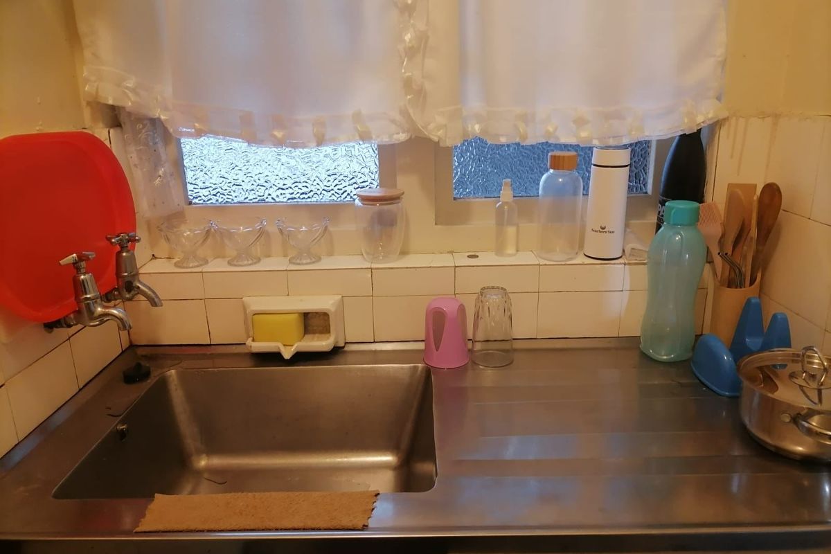 A compact kitchen sink area featuring a stainless steel basin, tiled splashback, and window access.