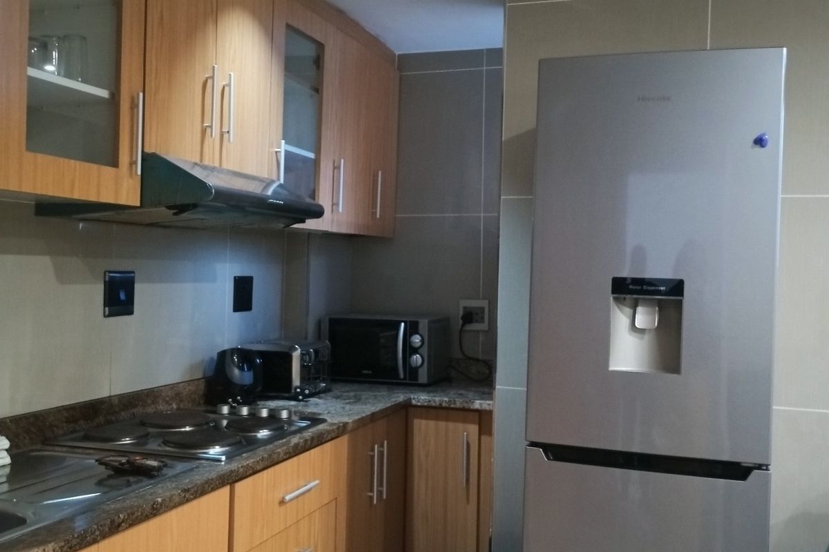 A functional kitchen featuring wood-finish cabinetry, granite countertops, an electric hob with extractor fan, and tiled wall finishes.