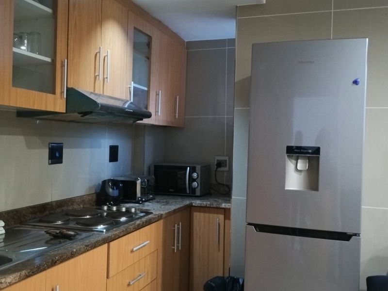 A functional kitchen featuring wood-finish cabinetry, granite countertops, an electric hob with extractor fan, and tiled wall finishes.