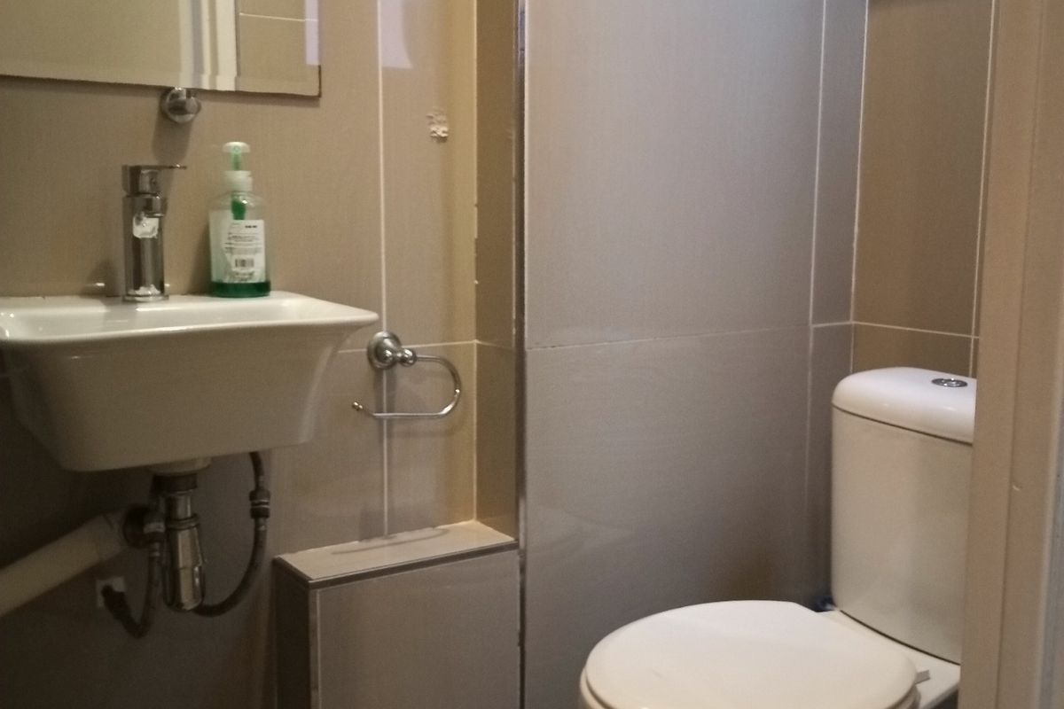 A compact bathroom featuring tiled walls and flooring, a wall-mounted basin with chrome fixtures, and a standard toilet.