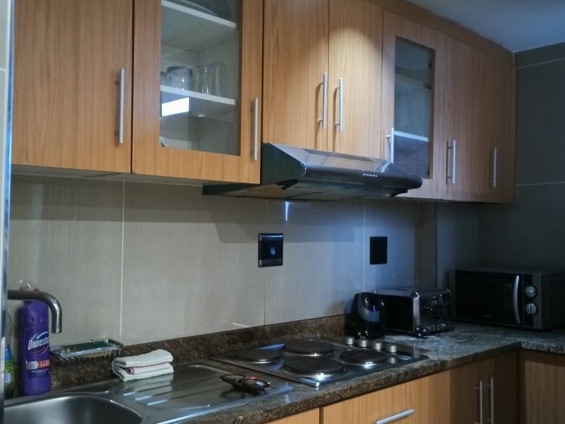 A functional kitchen featuring wood-finish cabinetry, granite countertops, a built-in electric hob with extractor fan, and a stainless steel sink.