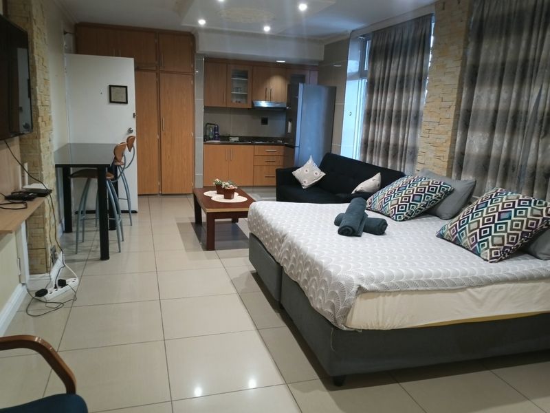 Open-plan studio apartment featuring a compact kitchen with built-in cabinetry, tiled flooring, and a stone-clad feature wall.