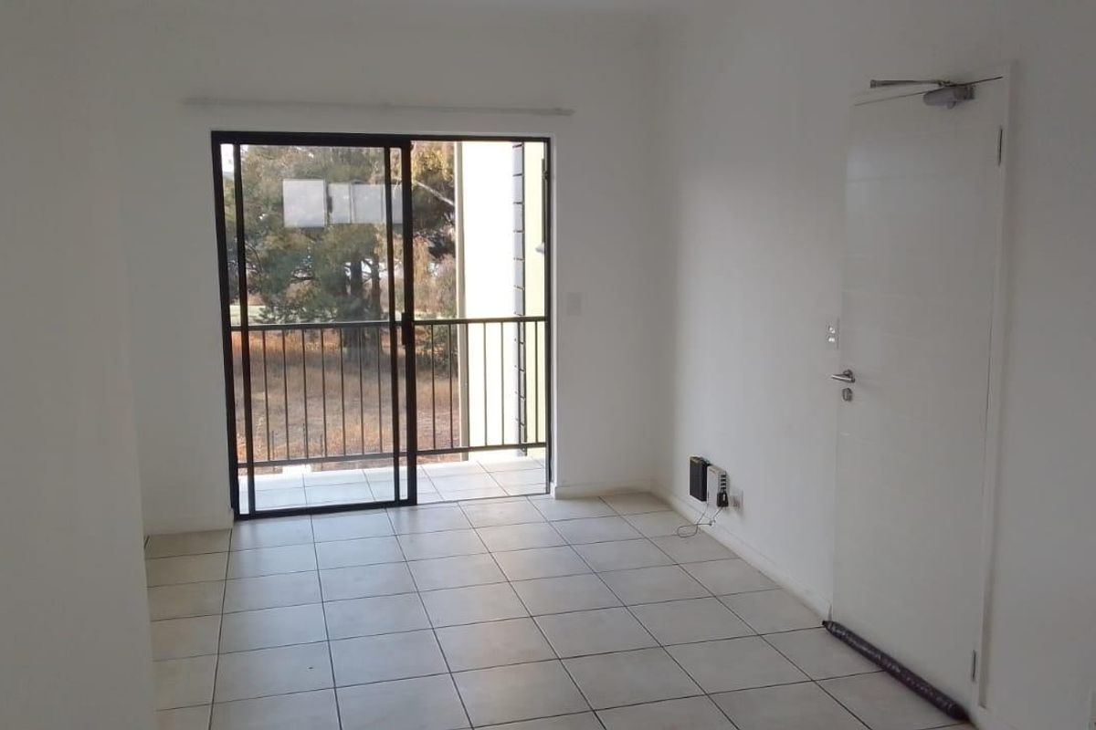An empty, neutrally painted living area featuring tiled flooring and a sliding glass door that opens onto a private balcony.