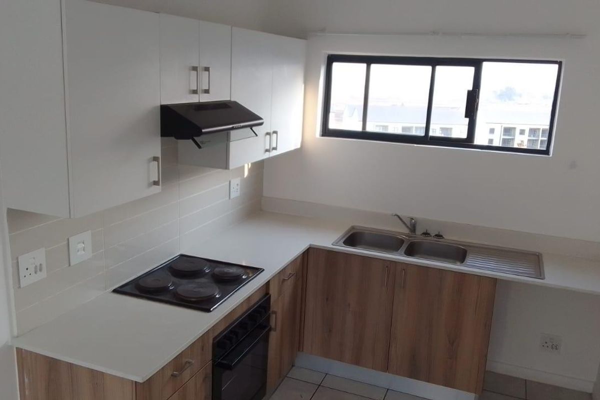 A clean, functional kitchen featuring modern wood-finish lower cabinetry, white upper cabinets, a built-in oven and hob, and a double bowl sink.