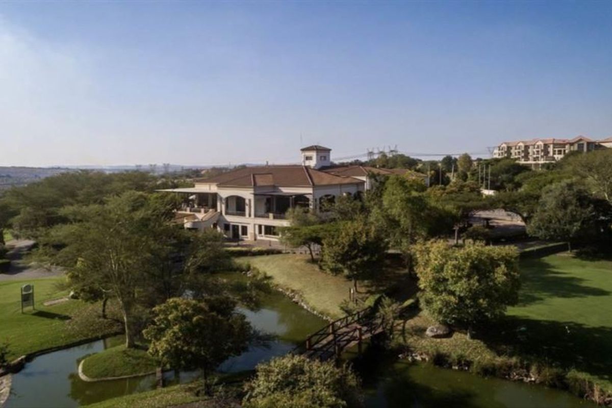 Aerial view of a residential property featuring landscaped grounds, a water feature, and a pedestrian bridge leading to the main building.