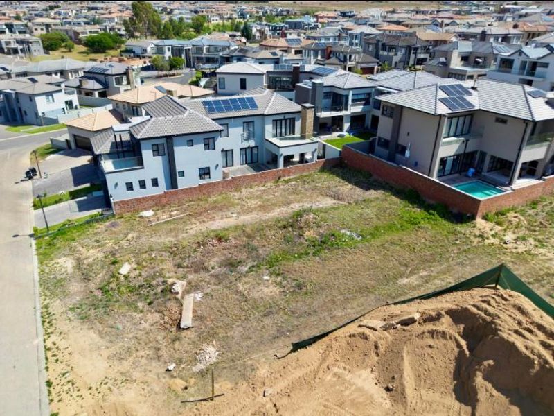 An aerial view of a vacant residential plot situated within a developed estate, featuring boundary walls and surrounding residential properties.