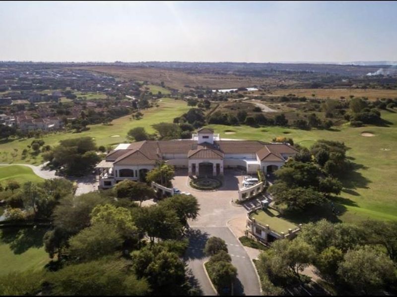 An aerial view of a large residential estate property featuring a paved driveway, tiled roof structure, and surrounding golf course landscape.