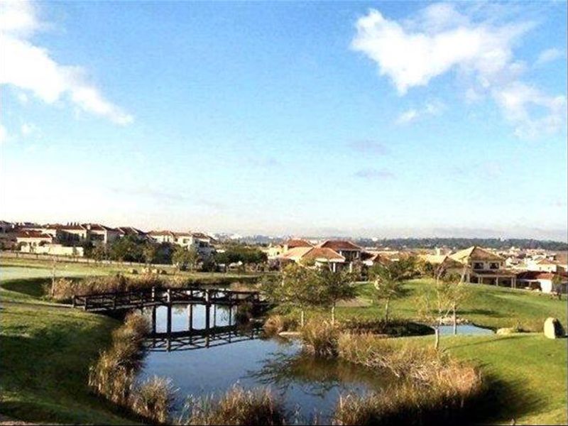 Scenic view of a landscaped pond with a wooden footbridge, set within a well-maintained residential estate and golf course environment.