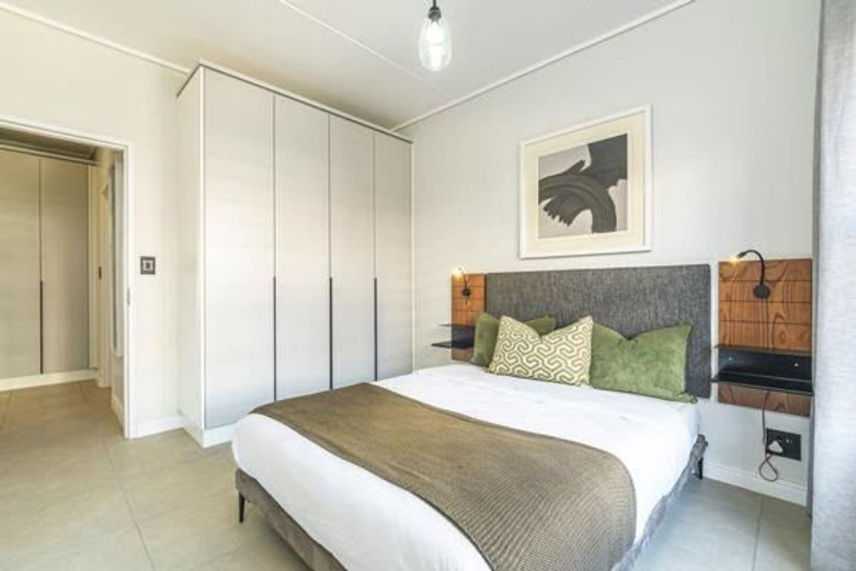 A well-maintained bedroom featuring built-in cupboards, tiled flooring, and modern wall-mounted bedside lighting with an integrated headboard design.