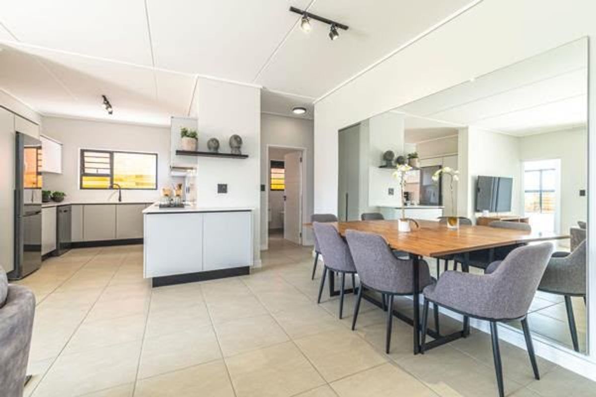 Modern open-plan living and dining area featuring tiled floors, a functional kitchen island, and a large wall mirror enhancing the sense of space.
