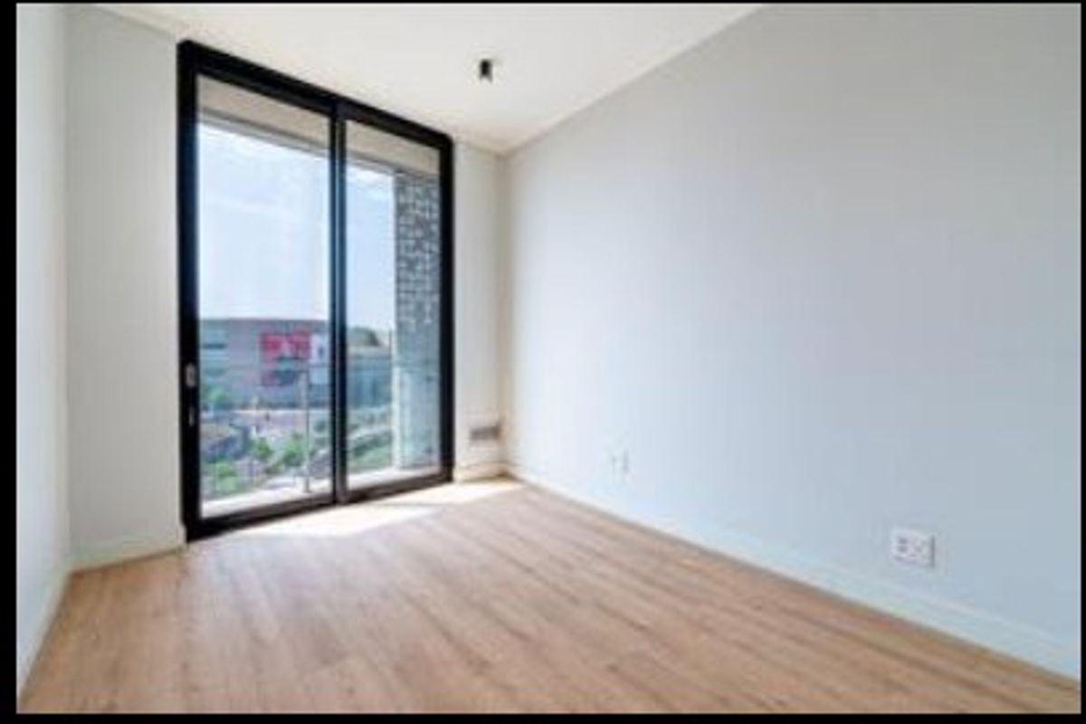 A bright, empty bedroom featuring light wood-look laminate flooring and a large sliding glass door providing access to an outdoor balcony.