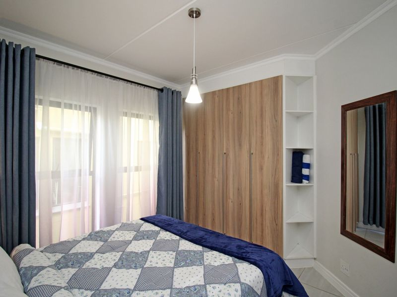 A well-maintained bedroom featuring modern wood-finish built-in wardrobes with integrated shelving, tiled flooring, and a contemporary pendant light fixture.