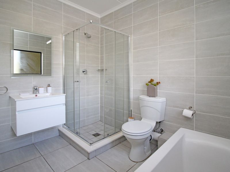 Modern bathroom featuring a wall-mounted vanity, glass shower enclosure, toilet, and bathtub with neutral floor-to-ceiling wall tiling.