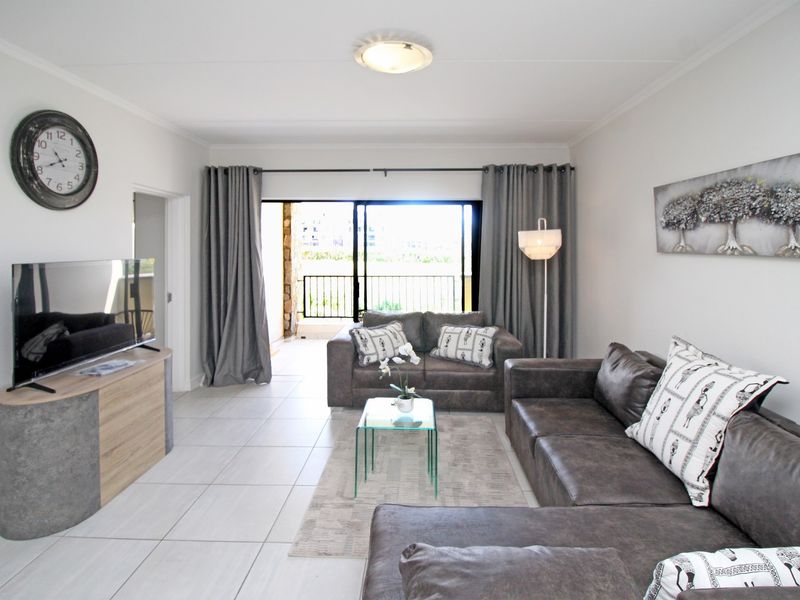 A bright and spacious living room featuring neutral tiled flooring, coved ceilings, and a large sliding glass door providing access to the balcony.