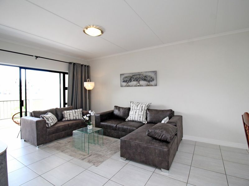 A bright living room featuring neutral tiled flooring and a large sliding glass door providing access to an outdoor balcony area.