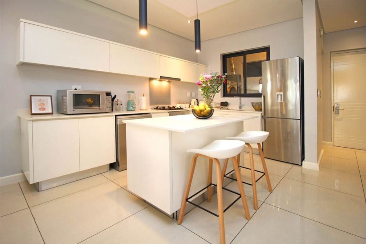 Modern kitchen featuring sleek white cabinetry, a central island with breakfast bar seating, stone countertops, and high-quality stainless steel finishes.