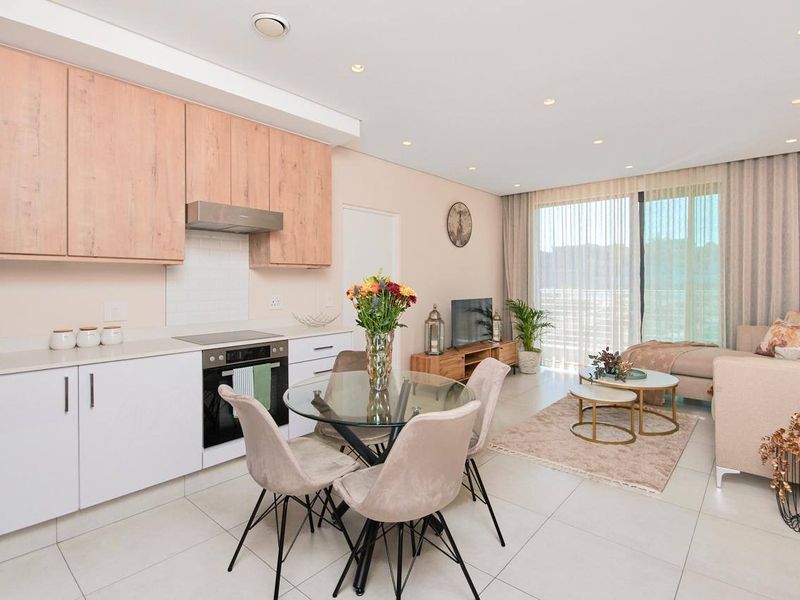 Modern open-plan living area featuring a sleek kitchen with light wood cabinetry, integrated appliances, and seamless flow to a bright, tiled lounge space.