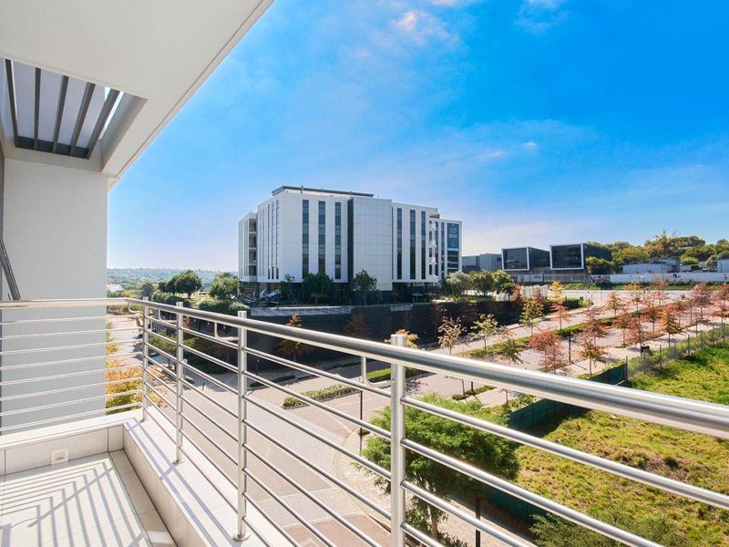 A modern balcony featuring a stainless steel balustrade and tiled flooring, offering an elevated view of the surrounding urban landscape.