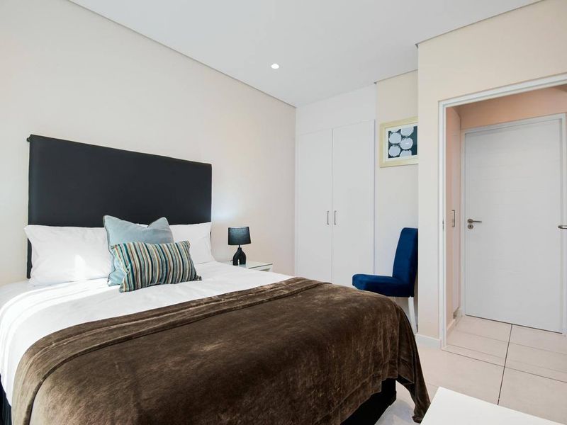 A well-maintained bedroom featuring built-in cupboards, neutral tiled flooring, and recessed downlighting, offering a clean and functional living space.