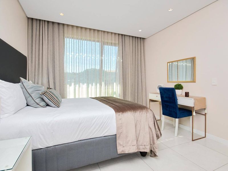 A well-maintained bedroom featuring neutral walls, tiled flooring, recessed lighting, and a large sliding glass door with floor-to-ceiling curtains.