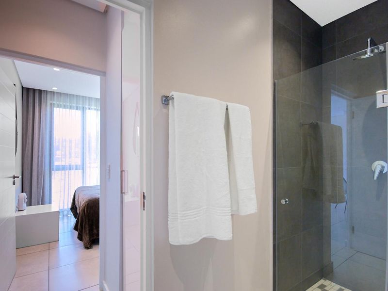 Modern bathroom featuring a glass-enclosed shower with dark tiling and a convenient towel rail, with a view into the adjacent bedroom.