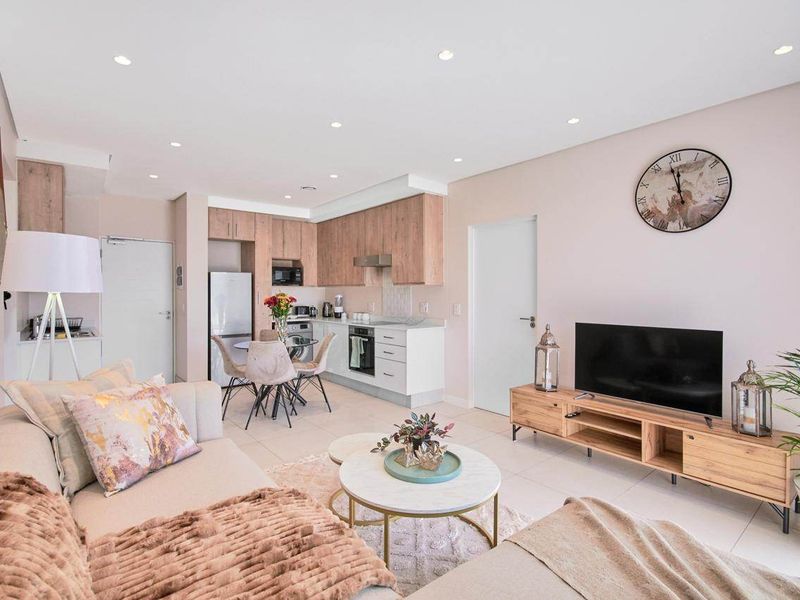 Modern open-plan living area featuring a contemporary kitchen with wood-tone cabinetry, stone countertops, and integrated appliances, seamlessly flowing into the lounge space.