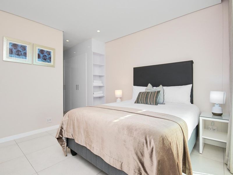 A modern, well-maintained bedroom featuring neutral tones, tiled flooring, built-in cupboards, and integrated shelving for storage.