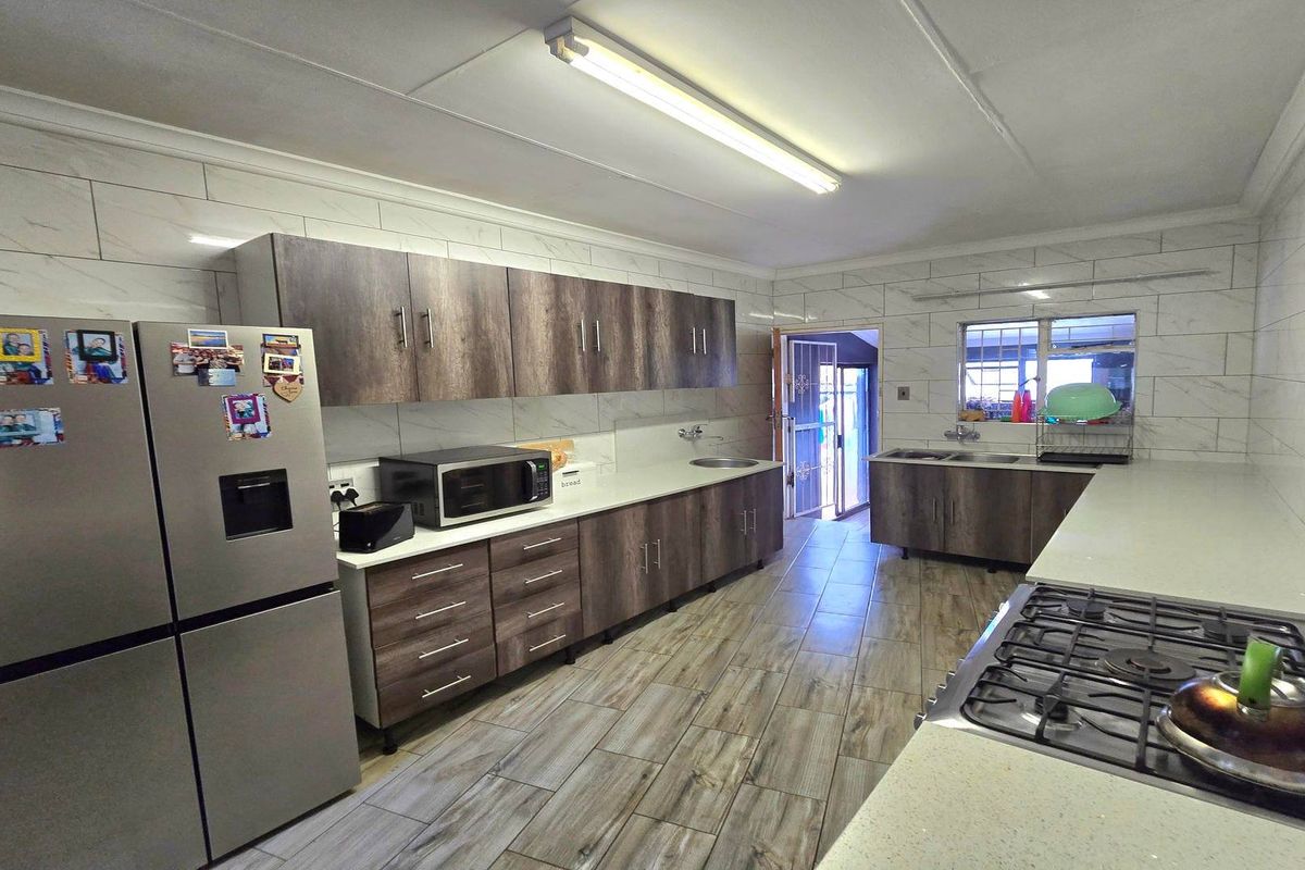 A functional kitchen featuring modern wood-look cabinetry, stone countertops, a gas hob, and tiled wall finishes with ample workspace.