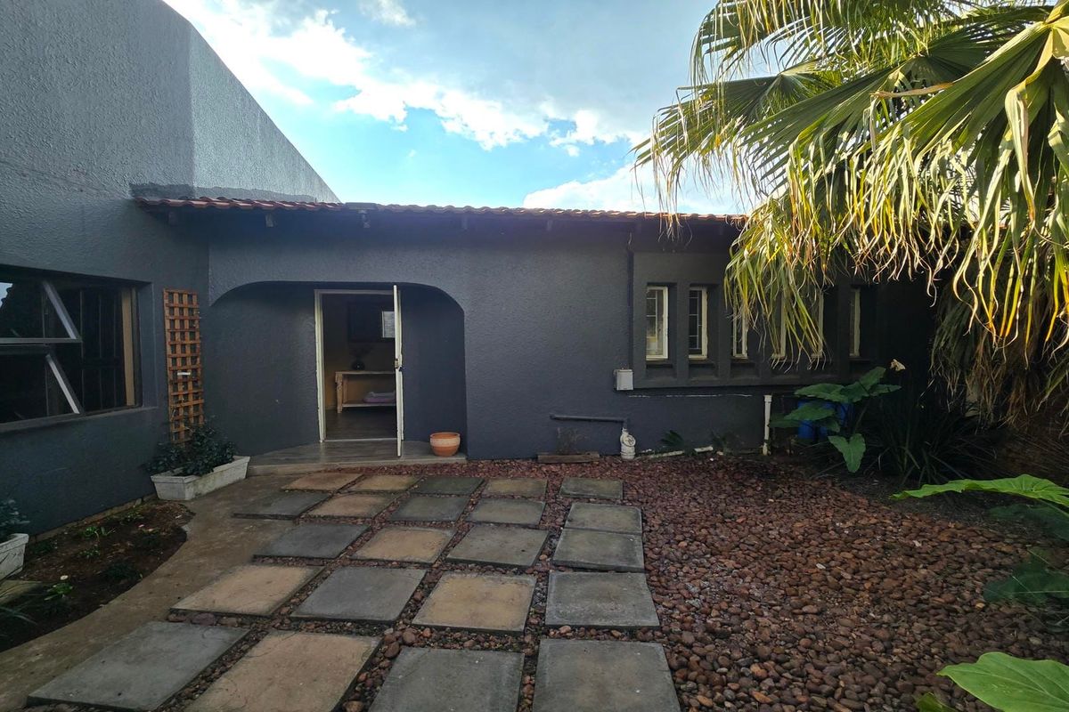 A rear exterior view of the house featuring a paved walkway, pebble garden, and an arched entrance leading into the home.