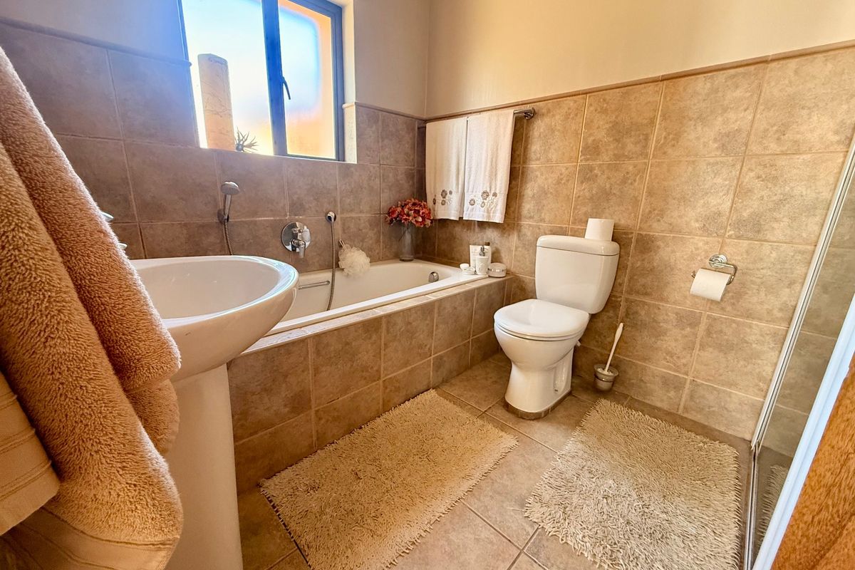 A functional bathroom featuring a pedestal basin, built-in bathtub with handheld shower, and toilet, finished with neutral wall and floor tiling.