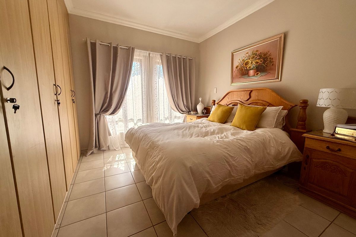 A well-lit bedroom featuring built-in wooden cupboards, neutral tiled flooring, and classic cornice detailing, offering a comfortable and functional living space.