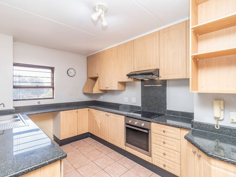 A functional kitchen featuring light wood cabinetry, granite countertops, built-in oven, electric hob, and tiled flooring.