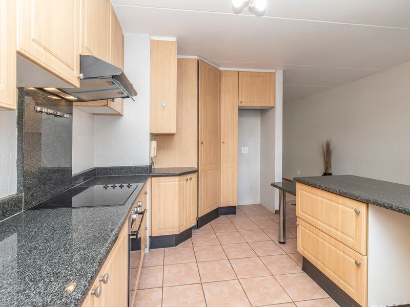 A functional kitchen featuring light wood cabinetry, granite countertops, a built-in oven, and an electric hob with an extractor fan.